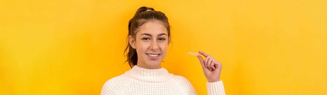 Woman Holding Invisalign Aligners In Front Of Yellow Background